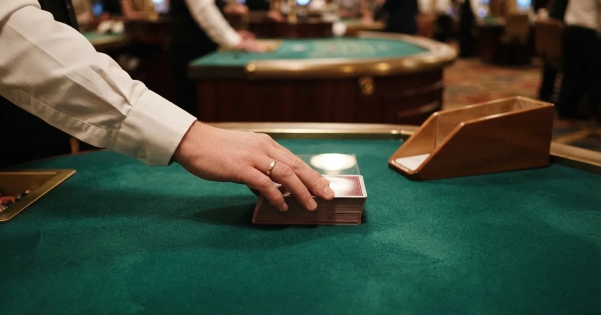 Croupierens händer blandar kort på grönt filt, taklampan speglas i den blanka kortbunten — casinon med störst vinstchans